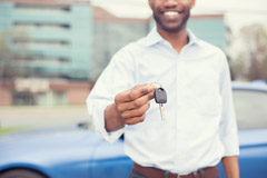 Smiling man holding car keys offering new blue car